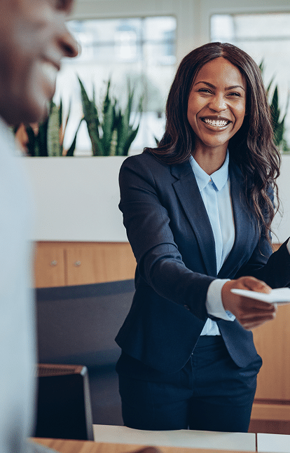 Femme d'affaires souriante : Accueil client professionnel Femme d'affaires noire souriante en costume bleu, remettant des documents à un client dans un bureau moderne. Accueil professionnel.